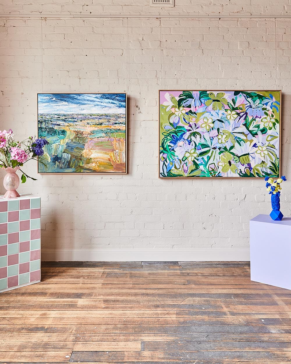 Two colorful paintings on a white brick wall with decorative elements.