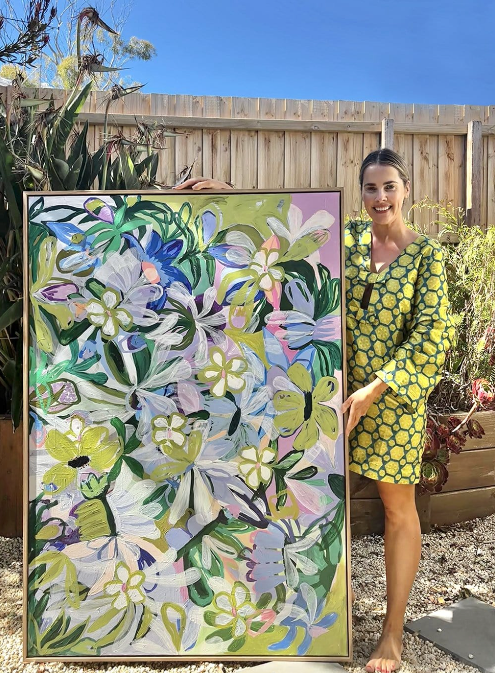 Woman in a yellow dress standing next to a large floral painting outdoors.