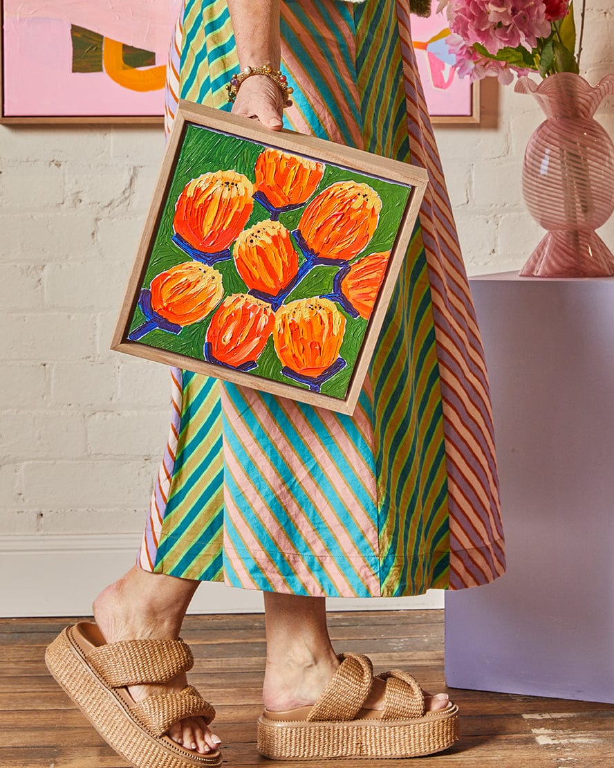 Person holding a framed painting of orange flowers in a colorful room.